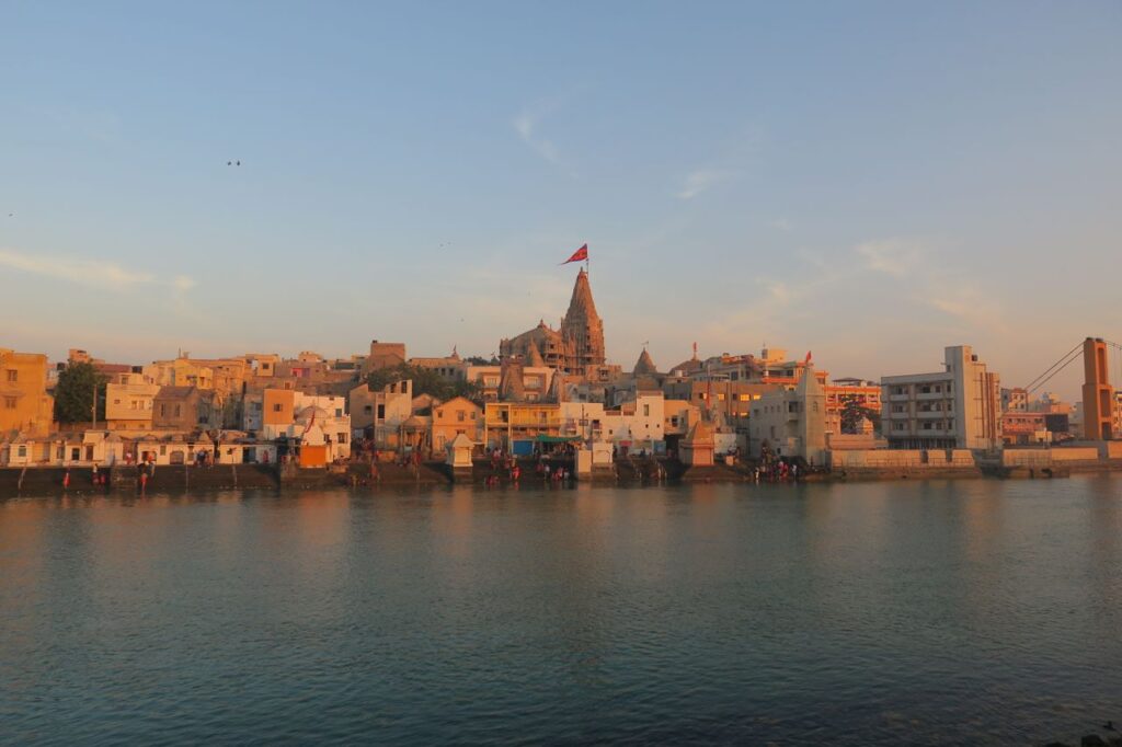 View of the historic Dwarka city and temple by the river at sunset, capturing its architectural beauty.